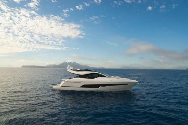 A luxurious white yacht glides through calm blue waters, with distant mountains and a partly cloudy sky in the background.